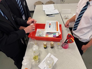 three students at a desk carrying out an experiment with a red tray and science equipmenttubes