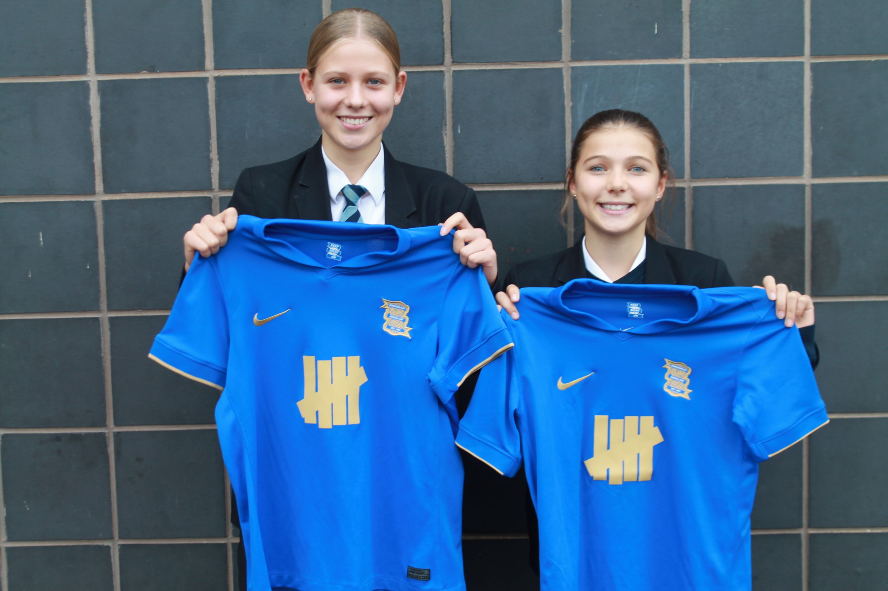 Two NLS students holding their blue Birmingham City shirts