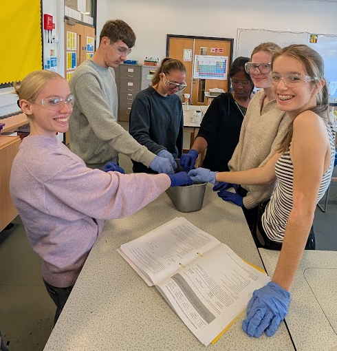 six students in a lab standing around an experiment on a  desk