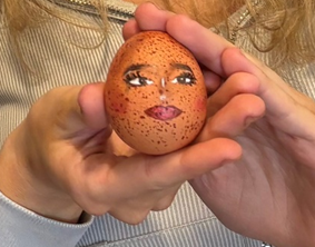  A pair of hand holding an egg which has had a face painted onto it