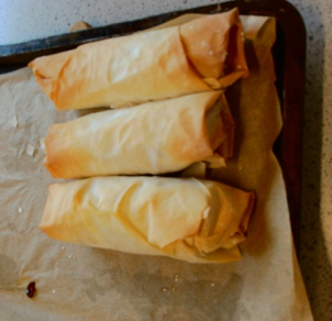 Photograph of three golden-brown baked pastry rolls placed on a baking tray lined with parchment paper. Pastry rolls appear crisp and evenly cooked, suggesting they are freshly baked and ready to serve.
