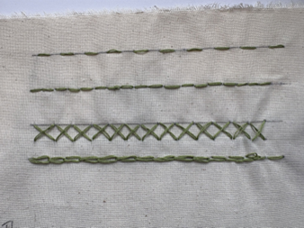 Photograph of four vertical rows of green embroidery stitches on beige fabric, showcasing different stitch patterns. Stitches vary from simple chain and running stitches to a more complex crisscross pattern, demonstrating basic embroidery techniques.