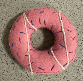 A pink donut with a hole in the center made from fabric with white threads across it