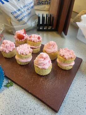 A group of cupcakes with pink icing  on a cutting board