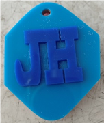 Photograph of a blue hexagonal keychain with a raised blue 3D-printed design with a JH stylised letter.