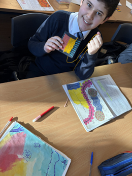 A child sitting at a table with a book and pen and making a weave