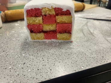A cake with a checkered pattern on it in pink and yellow with white icing