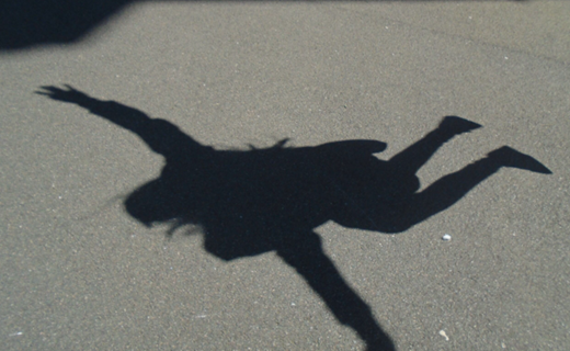 Photograph showing shadow of a person jumping  with arms and legs spread out on a paved surface. Shadow details include outstretched fingers  suggesting dynamic movement.