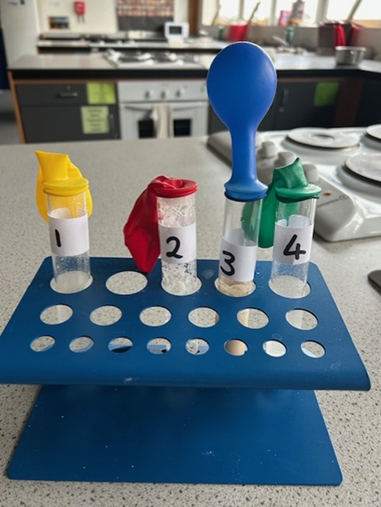 A blue stand with four tubes with different coloured balloons