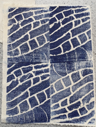 A photograph of a textile piece featuring a block print pattern of blue and white abstract brick-like shapes arranged in a grid of four sections. Each section shows variations in ink coverage and texture