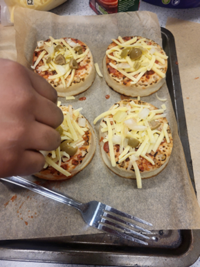 A tray with four pizzas on, a hand sprinkling cheese and a forknd holding a fork over small pizzas