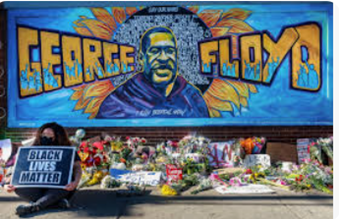 A person holding a sign next to a sign  of George Floyd with flowers in front of the sign