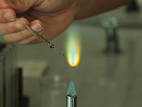 A hand holdinga  wore over a bunsen burner and creating a  blue and yellow flame