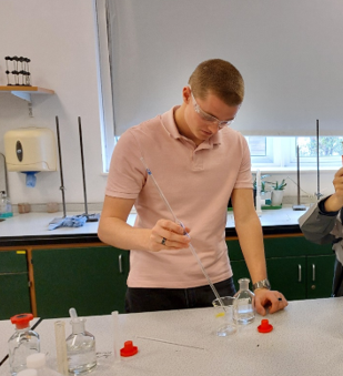 A STUDENT WEARING GOGGLES CARRYING OUT AN EXPERIMENT IN A LAB 
