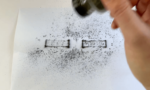 a white piece of paper with iron filings on with two solid rectangle shaped outlines 