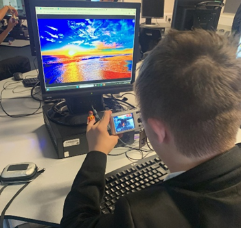 A student  sitting at a desk with a computer loading photographs which he is editing