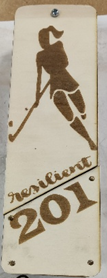 Photograph of a wooden plaque featuring a silhouette of a female field hockey player and the word "resilient" above the yea