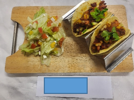 A wooden cutting board with tacos and salad