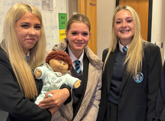 three students holding a doll
