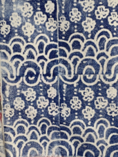 Photograph of a fabric featuring a repeating pattern of white floral shapes and curved wave-like lines on a dark blue background. The design is symmetrical with vertical alignment