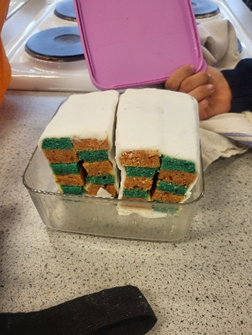Two cakes in a glass container with a checkered pattern on it in green and yellow with white icing