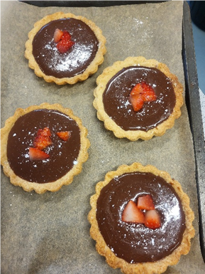 A group of four chocolate tarts with strawberries on top