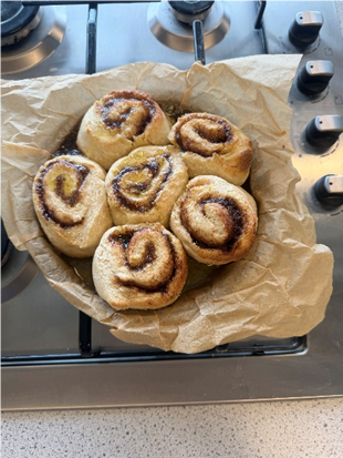  photograph showing a gas stovetop with four control knobs and a burner covered by crumpled brown parchment paper. Six cinnamon roll are on the parchment paper 