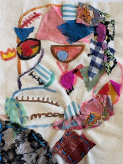 a  mixed-media textile artwork featuring an abstract face composed of various fabric scraps and stitched elements on a beige background. The face includes colorful patches in pink, blue, green, and floral patterns, with embroidered details outlining facial features and adding textur