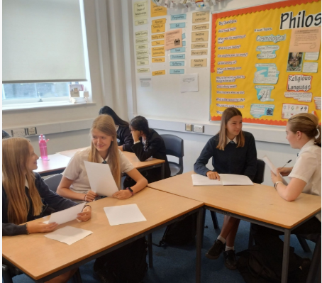 four students sitting at tables interviewing each other working in pairs
