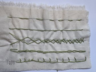 Photograph of a fabric sample displaying five vertical rows of different green embroidery stitches, each row demonstrating a stitch pattern