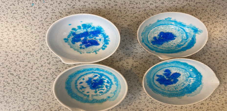 Four ceramic bowls with blue and turquoise abstract swirl patterns are arranged on a speckled countertop. Each bowl features unique variations of circular designs with a mix of darker and lighter blue shades.