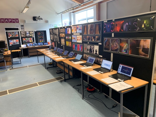 A photography classroom with tables, and laptops  displaying the A Level work