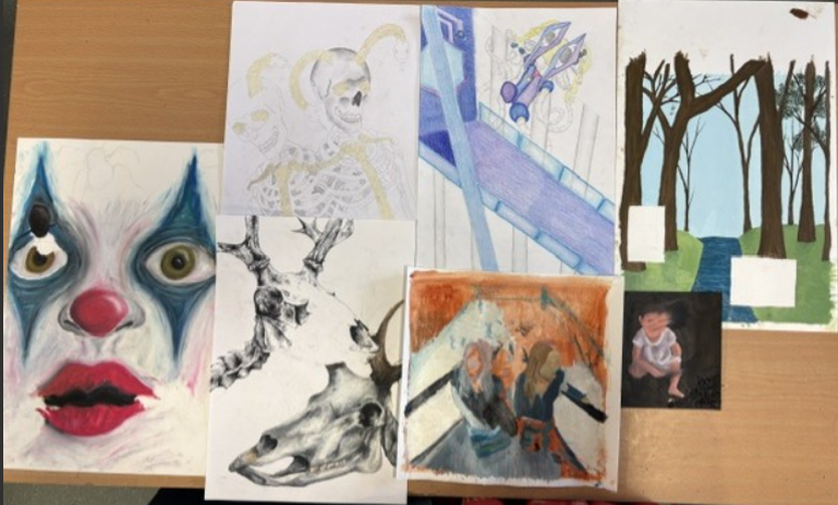A photograph showing seven diverse artworks arranged on a wooden surface, featuring a mix of abstract, anatomical, and landscape themes. Notable elements include a close-up of a face with exaggerated eyes and lips, a detailed skeletal drawing, a futuristic scene with geometric shapes, and a stylised forest with bare trees and green patches.