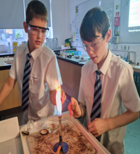 two students in a lab completing flame tests at a bunsen burner