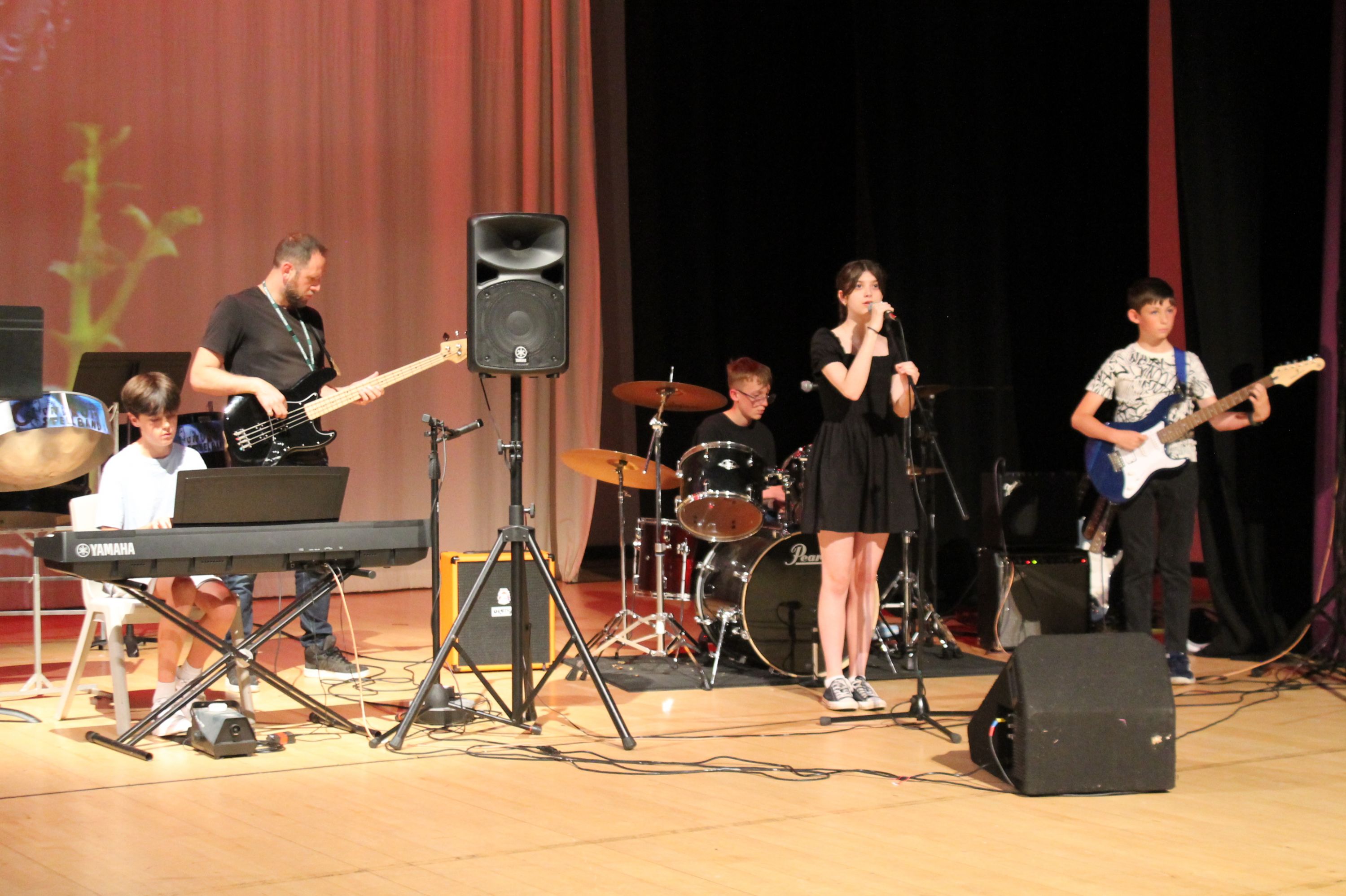 four students and their teacher playing  keyboard, drums, 2 x guitar and singing in the rock band
