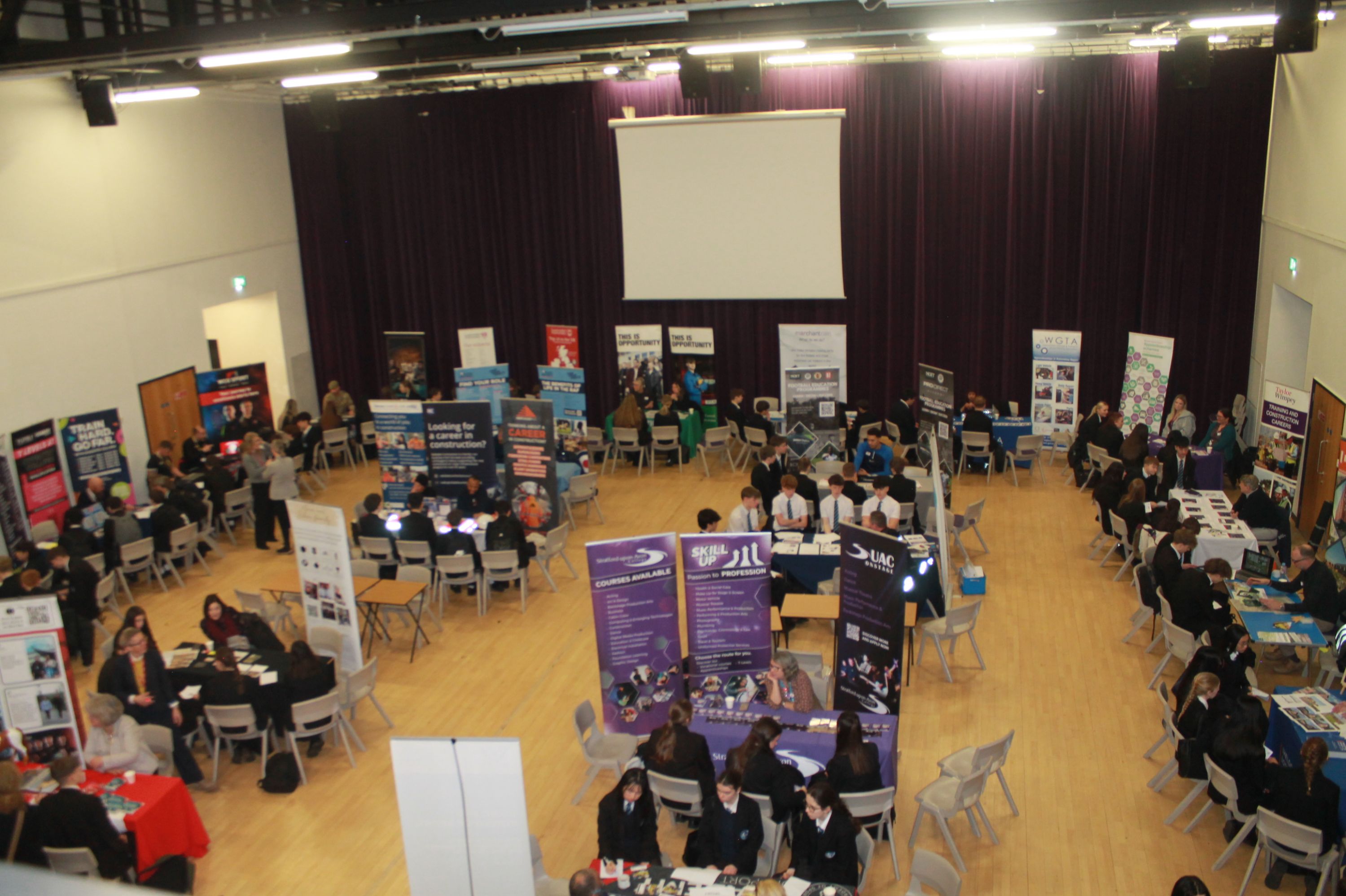 The careers fair in  the theatre with many chairs , tables and a projector screen