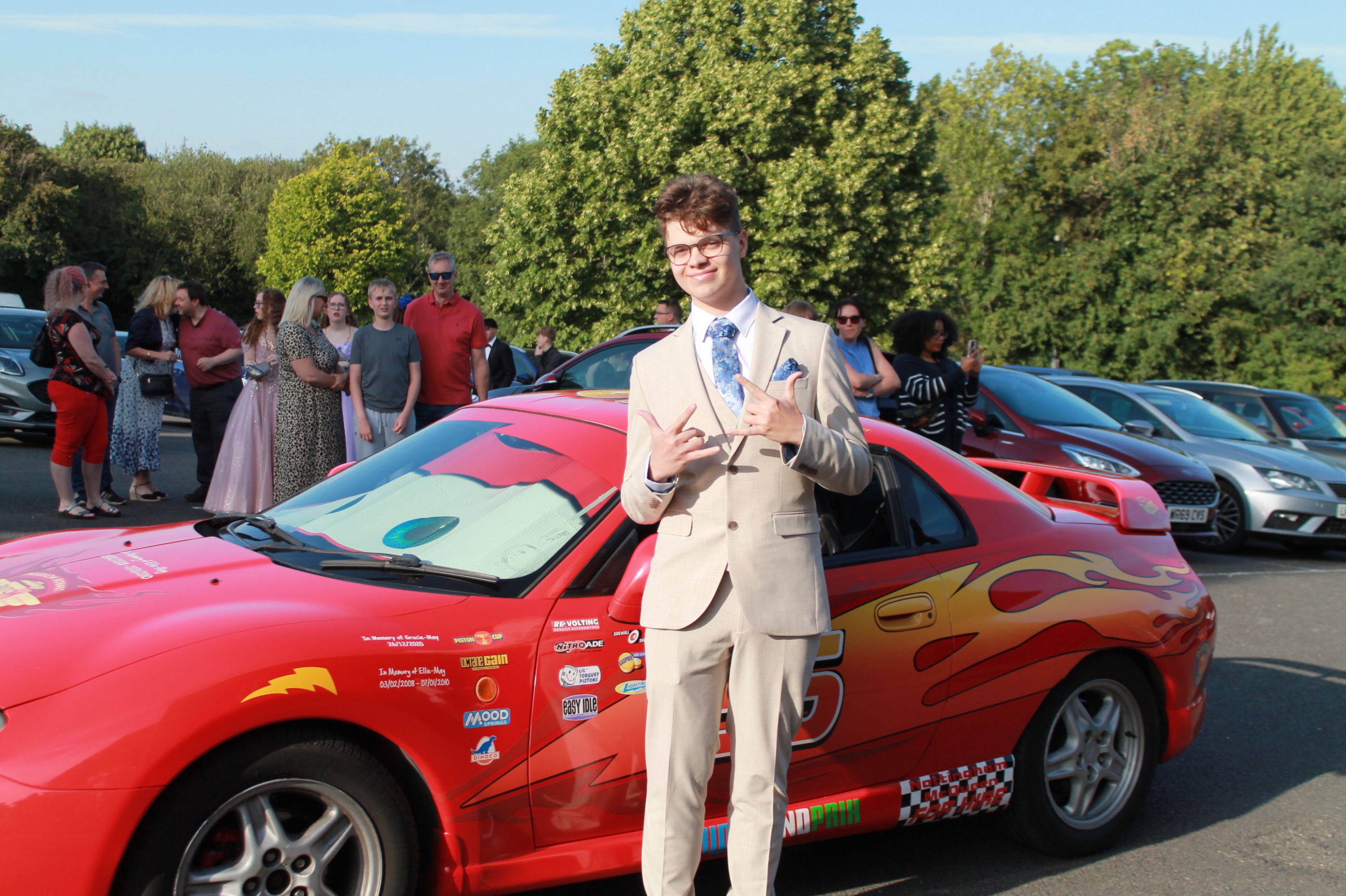 a student at prom standing by a  red car 