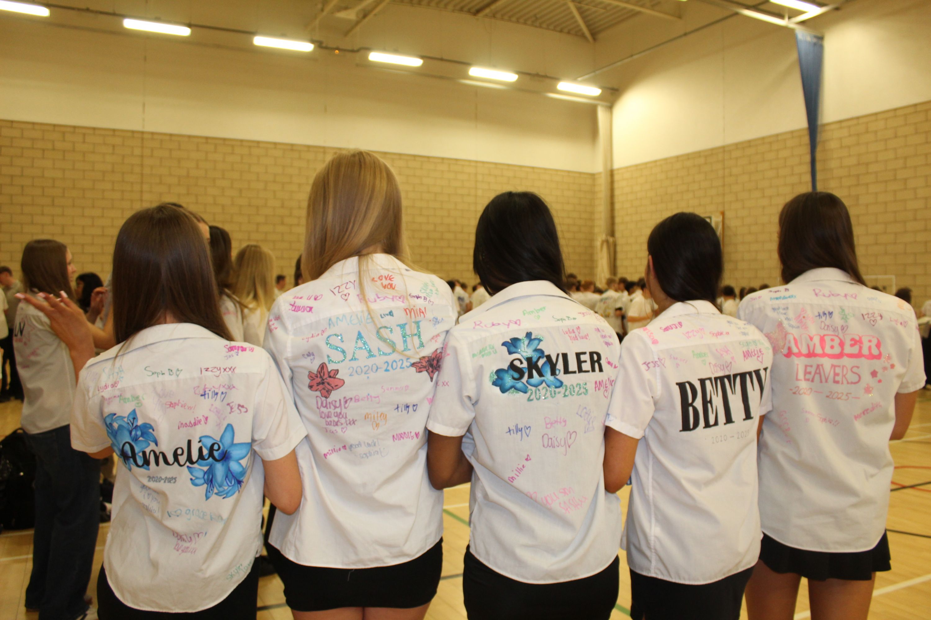 Fiove studnets showing the backs of their shirts with their names and signings