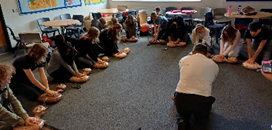 A group of people kneeling on the floor learning CPR on models