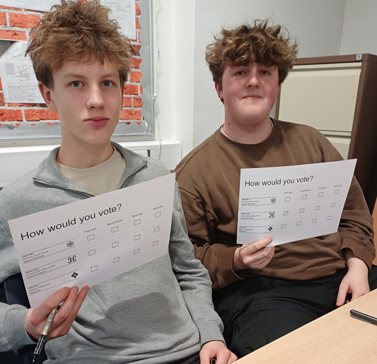 2 students sitting at desk holding voting cards 