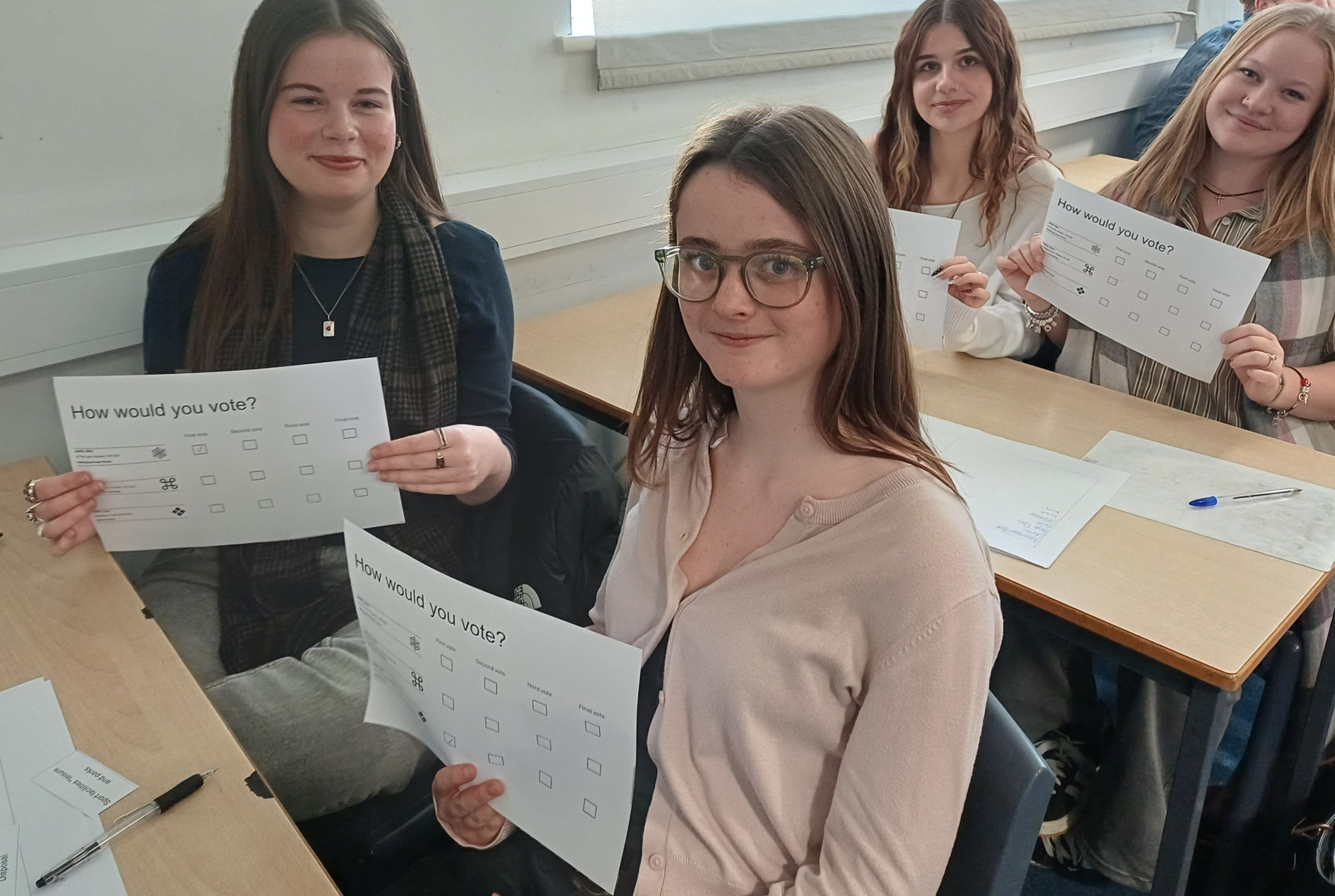 4 students sitting at desk holding voting cards 