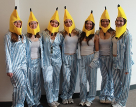 Photograph of seven people standing side by side wearing blue and white striped pyjamas and banana-shaped hats