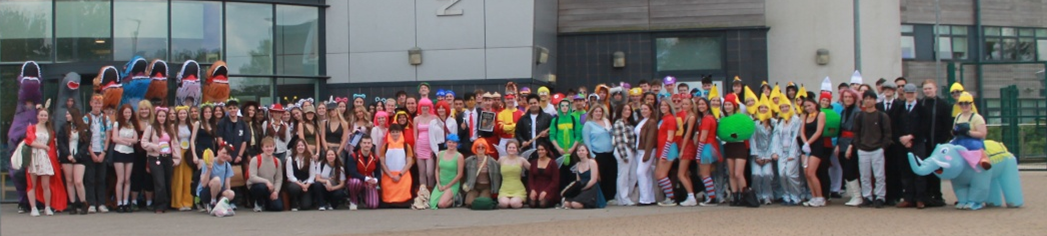 Photograph of a large group of people dressed in various colourful costumes posing outside a modern building with "North Leamington" signage. Costumes include characters from cartoons, animals, and superheroes