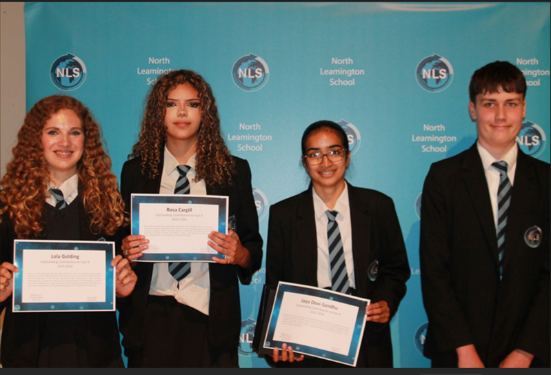 Photograph of four North Leamington School students standing in front of a branded backdrop, three holding certificates. Students wear school uniforms with blazers and striped ties, indicating an awards or recognition event.