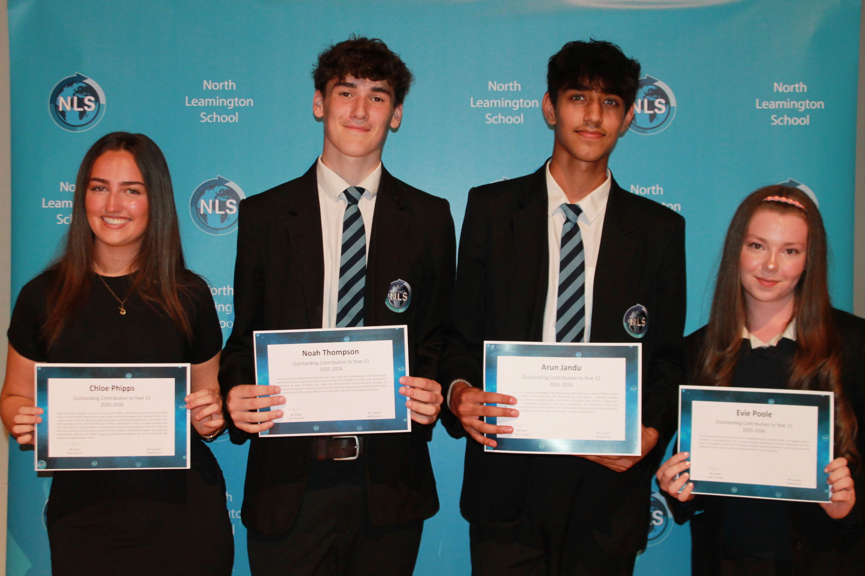 Photograph of four students standing in front of a blue North Leamington School backdrop, each holding a certificate. Students wear school uniforms, with three boys in blazers and ties and one girl in a black dress, highlighting an awards or recognition event.