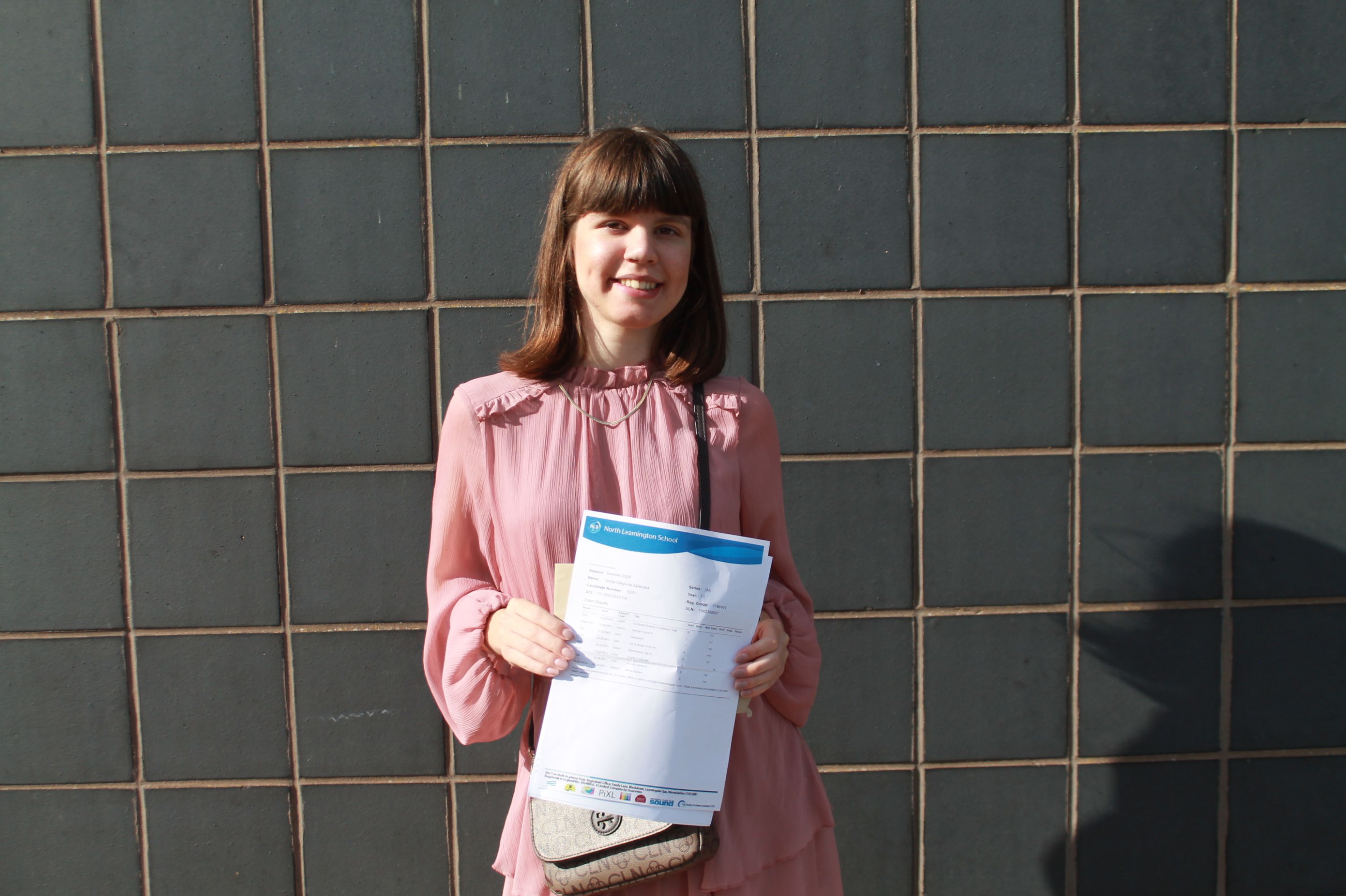 Photograph of a young women standing side by side against a tiled wall, each holding documents or envelopes