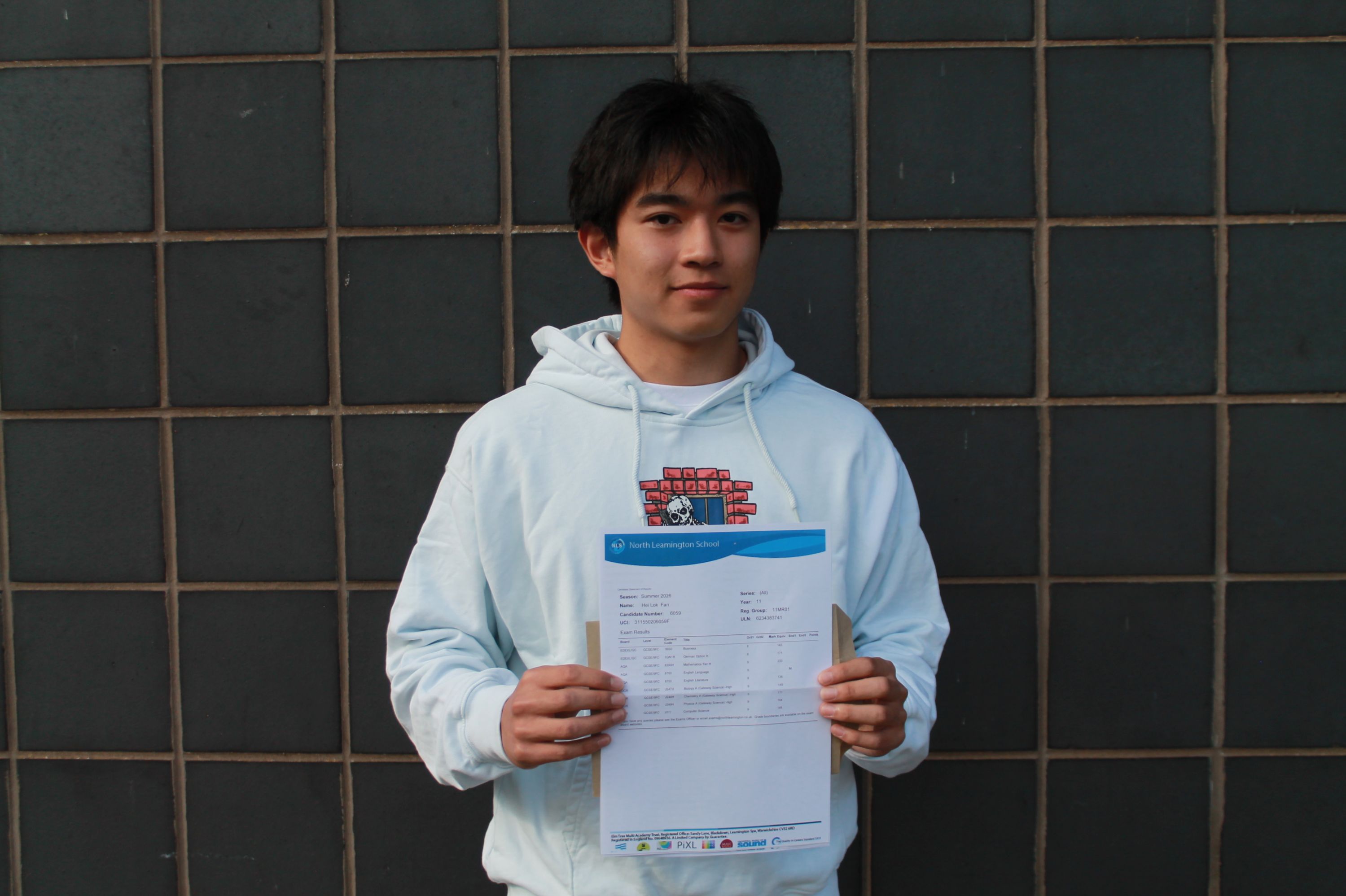Photograph of a young man standing against a tiled wall, each holding documents or envelopes