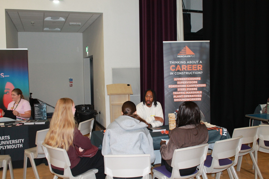 4401 Photograph shows a career stand where three students speak with representatives. Banners promote construction careers, apprenticeships and progression to supervisory or foreman roles, while tables display information materials.