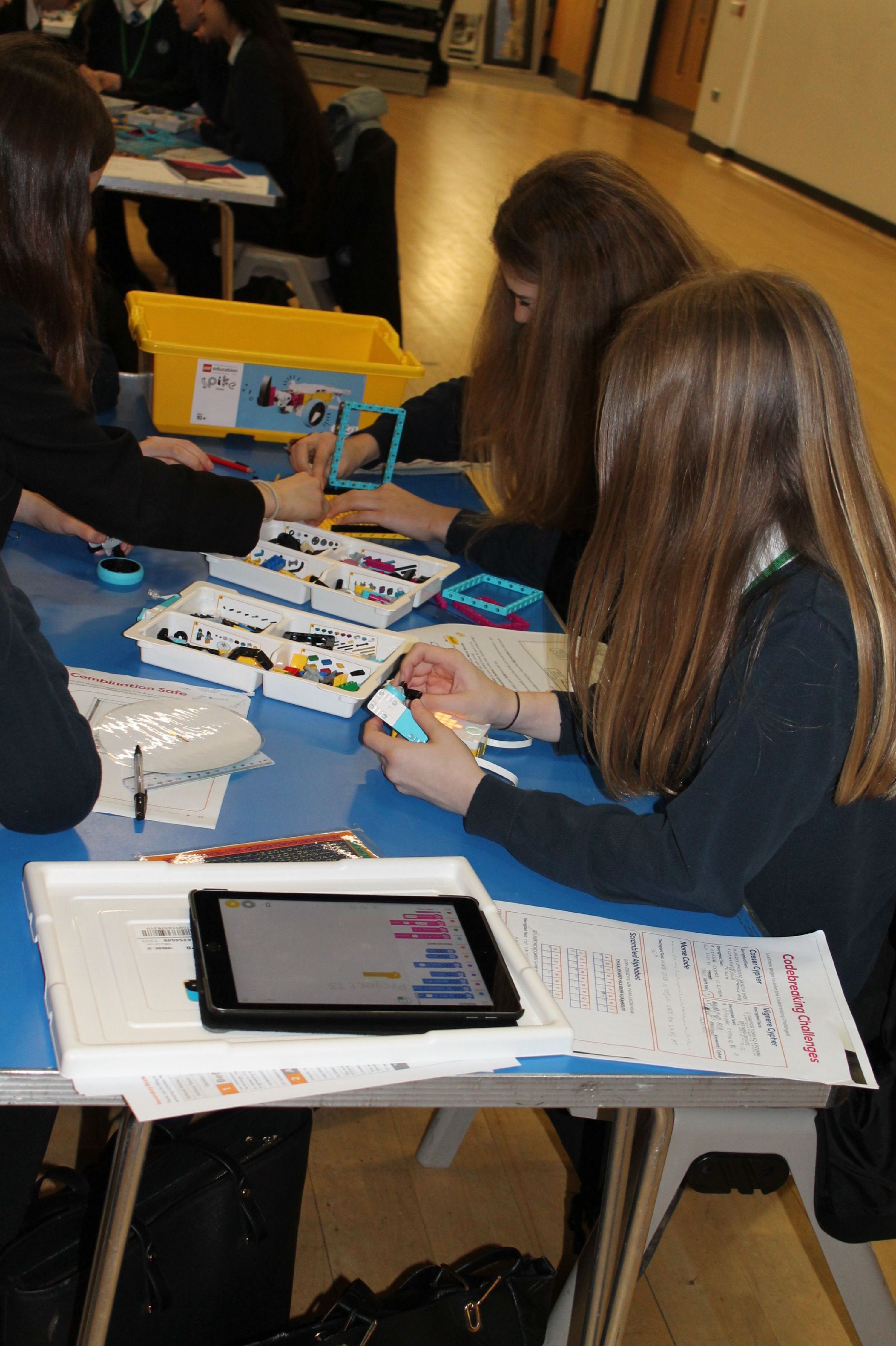 three girls sitting at a table building a  model