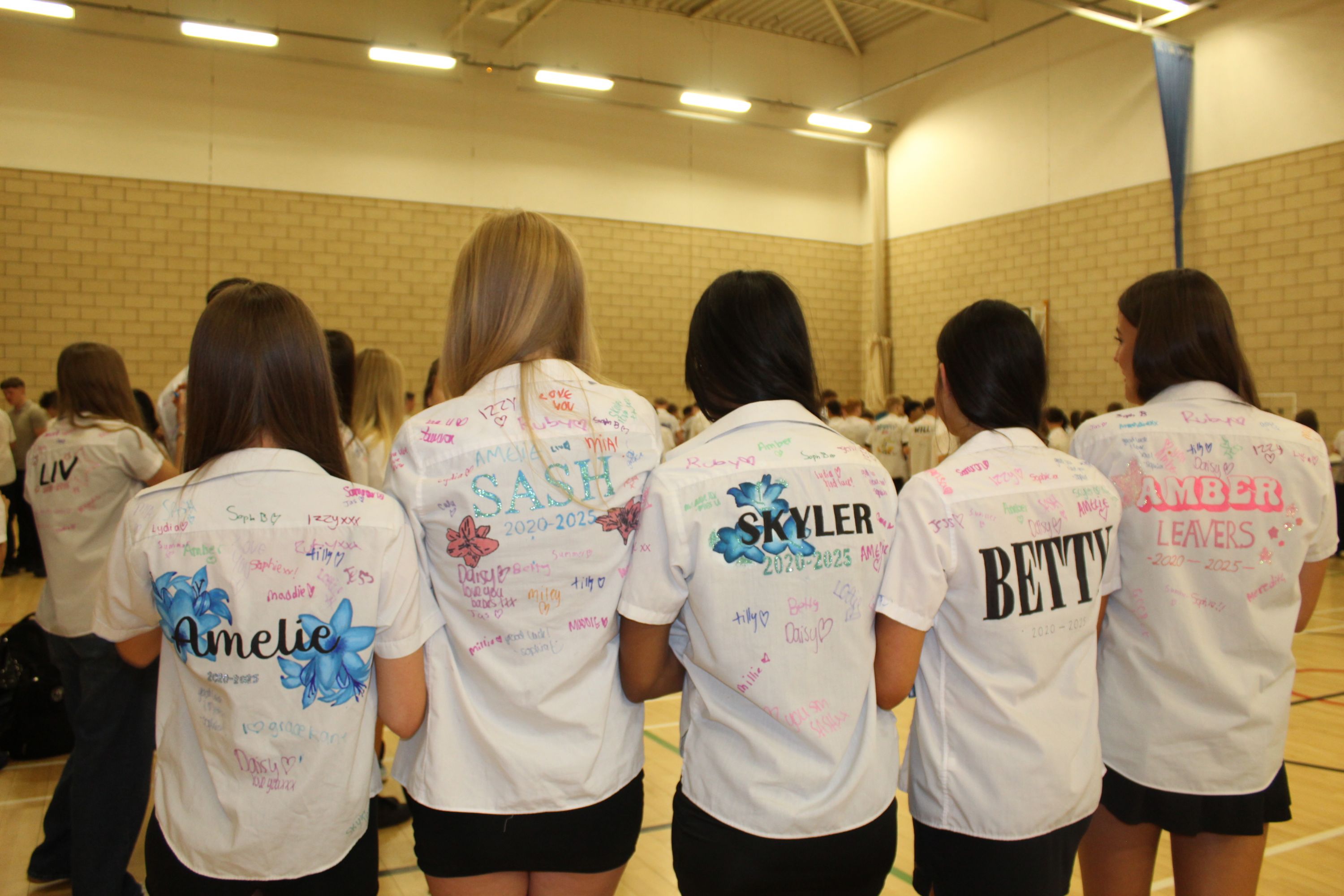 five students in a line showing the back of their decorated shirts